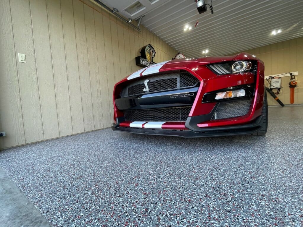 A red sports car with the label "GT350" in a clean garage with a speckled floor. A wall with a logo decorates the background.