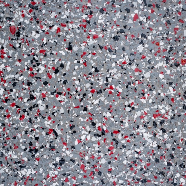 The image shows a close-up of a terrazzo floor with a speckled pattern of red, black, white, and gray fragments embedded in a gray matrix.