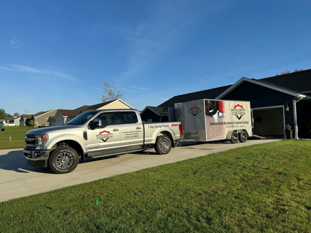 A silver pickup truck with company decals is towing a matching trailer parked in a residential driveway on a sunny day.
