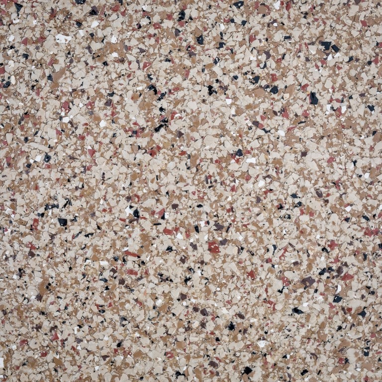 This image shows a close-up of a speckled surface, possibly a countertop or floor, with a variety of small, irregularly shaped pieces in beige, black, and red tones.