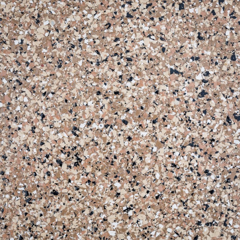 The image shows a close-up of a speckled beige surface, likely a terrazzo or aggregate flooring, with an assortment of small, multicolored stone fragments.